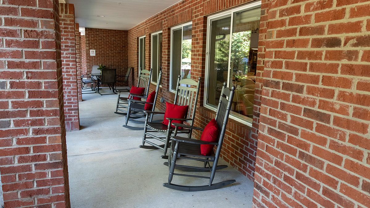A row of rocking chairs with red cushions lined up on a brick porch.