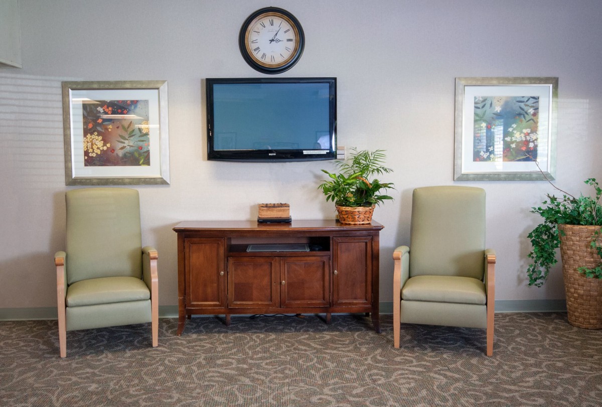A well-organized waiting room with two chairs, a television, and a clock on the wall.