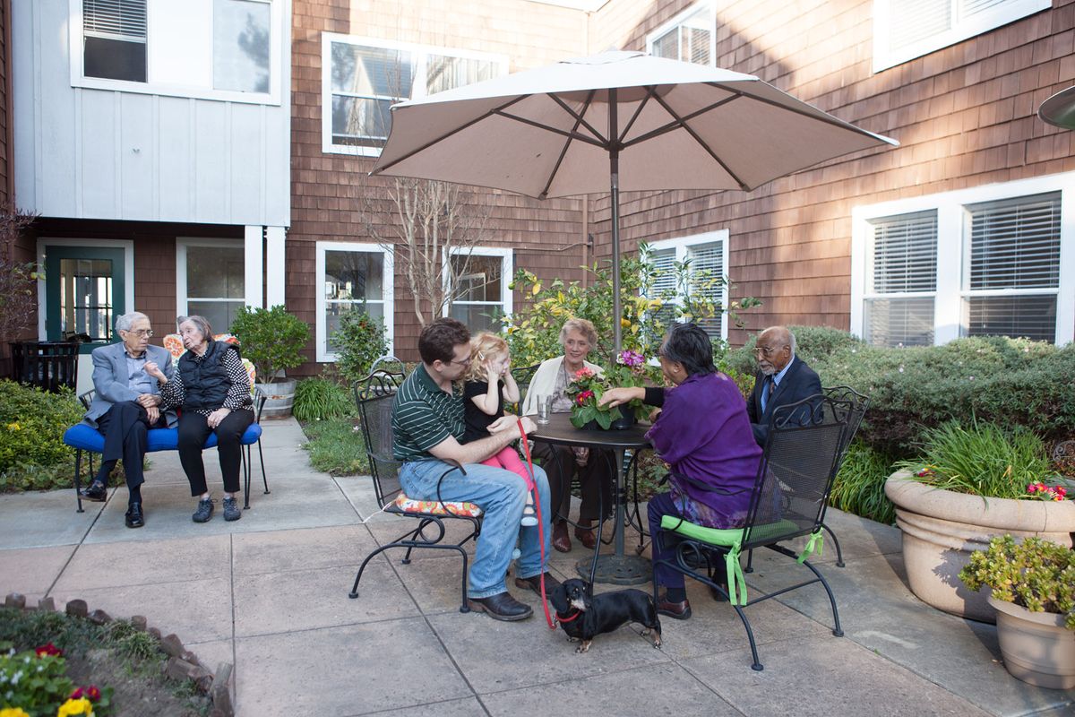 A group of people socializing on a patio under an umbrella.