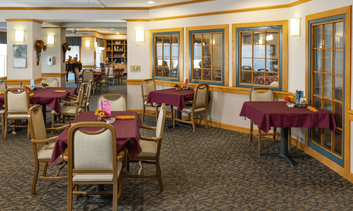 A well-lit dining area with tables and chairs, featuring maroon tablecloths and elegant decor.