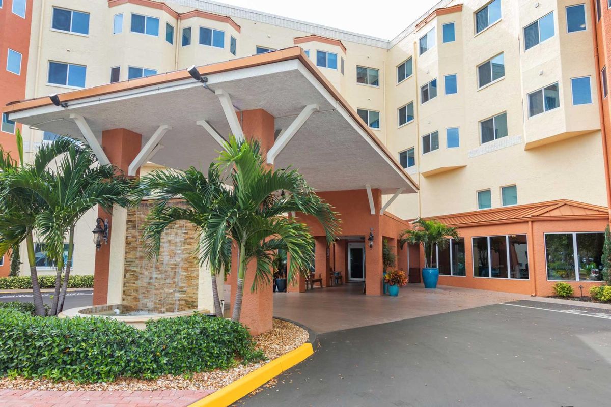 A modern building entrance with palm trees and a covered driveway.