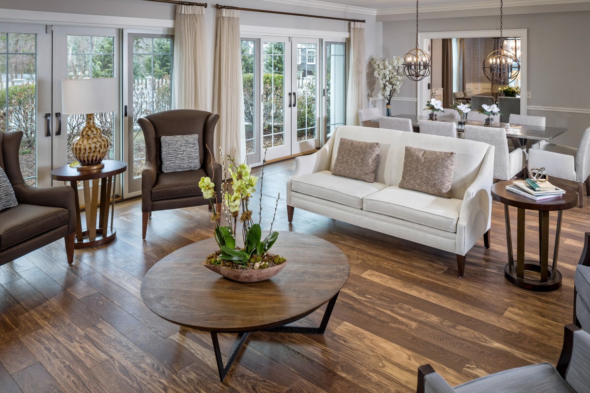 A beautifully designed living room with a white sofa, wooden coffee table, and large windows.