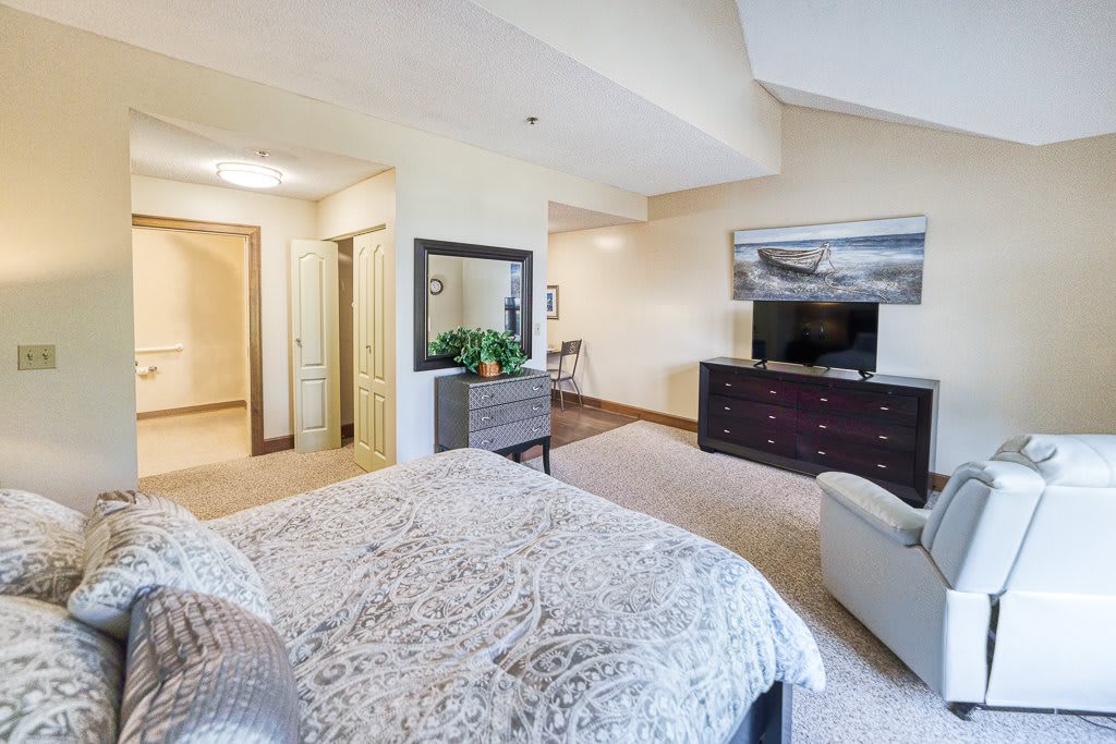 A spacious bedroom with modern furnishings, featuring a large bed, dresser, mirror, and television.
