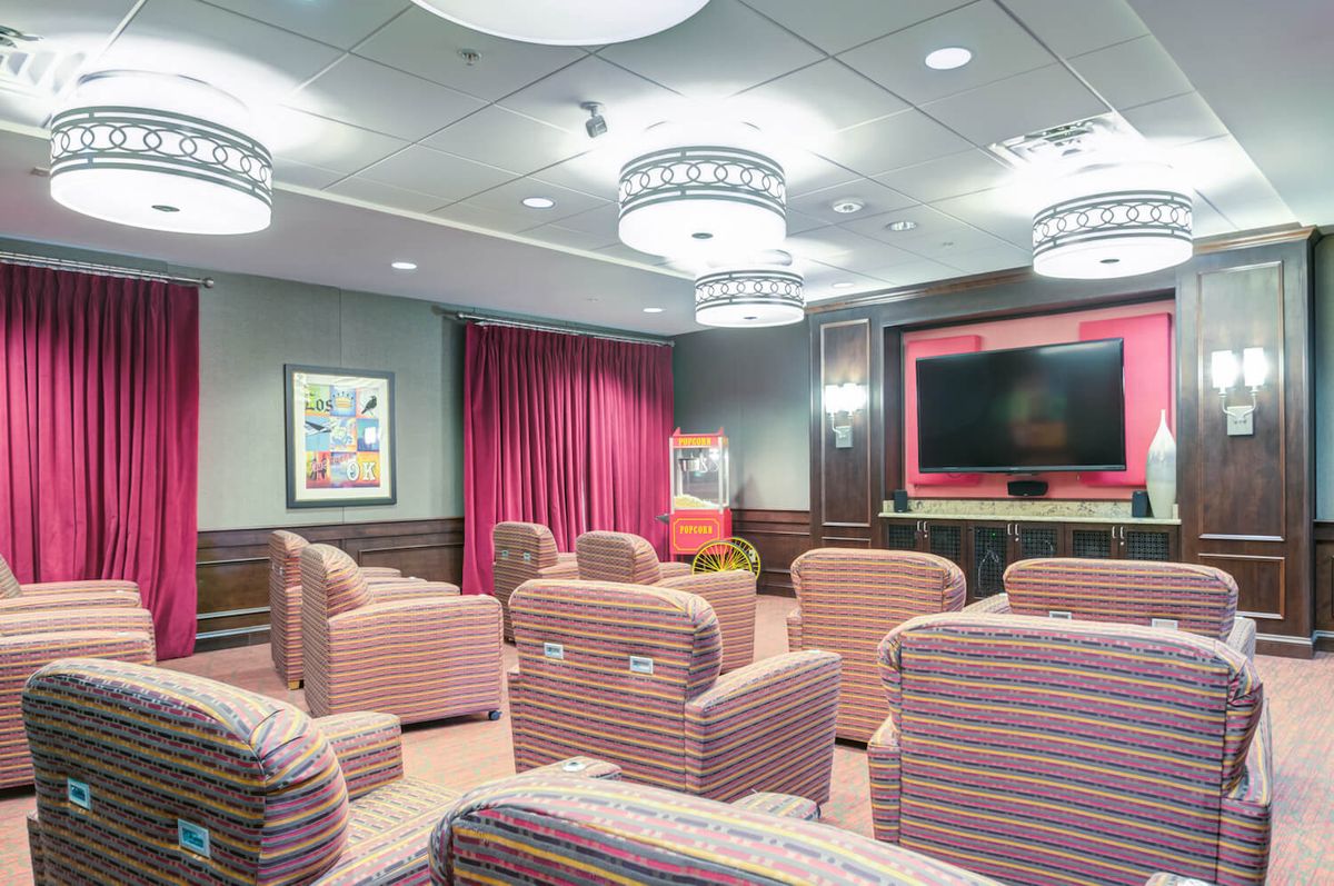 A cozy theater room with plush seating and a large screen, elegantly decorated with chandeliers and rich drapery.