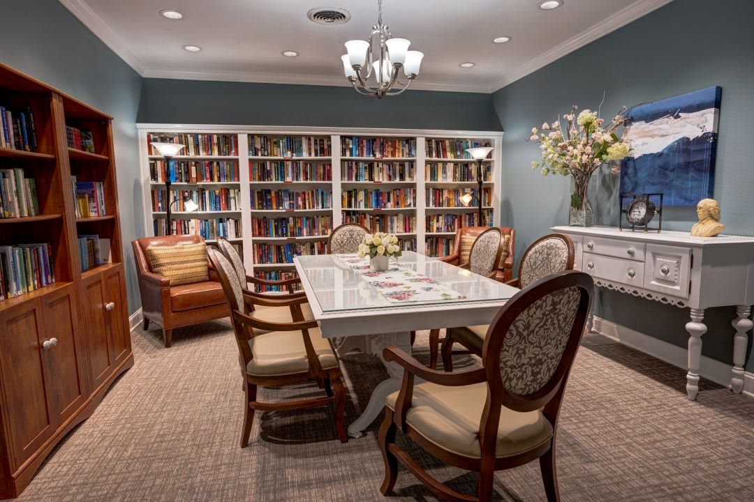 A cozy library with a central table surrounded by comfortable chairs, lined with bookshelves and adorned with a floral centerpiece.