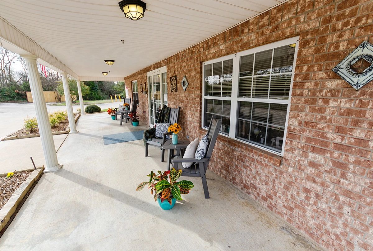 A cozy porch with brick walls, adorned with chairs and plants under a covered patio.