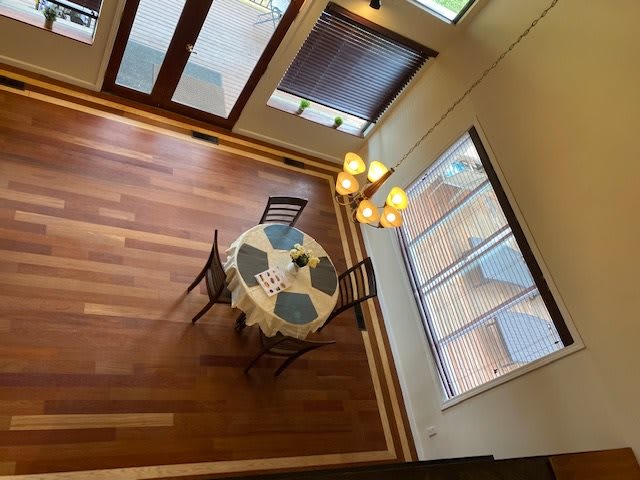 A cozy dining area with wooden flooring, featuring a round table and chairs, illuminated by a chandelier.
