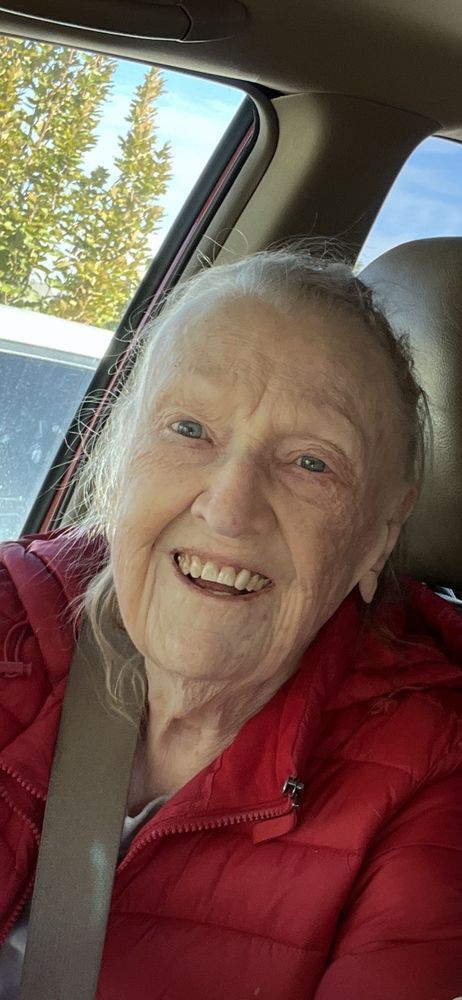 An elderly woman smiling while seated in a car.
