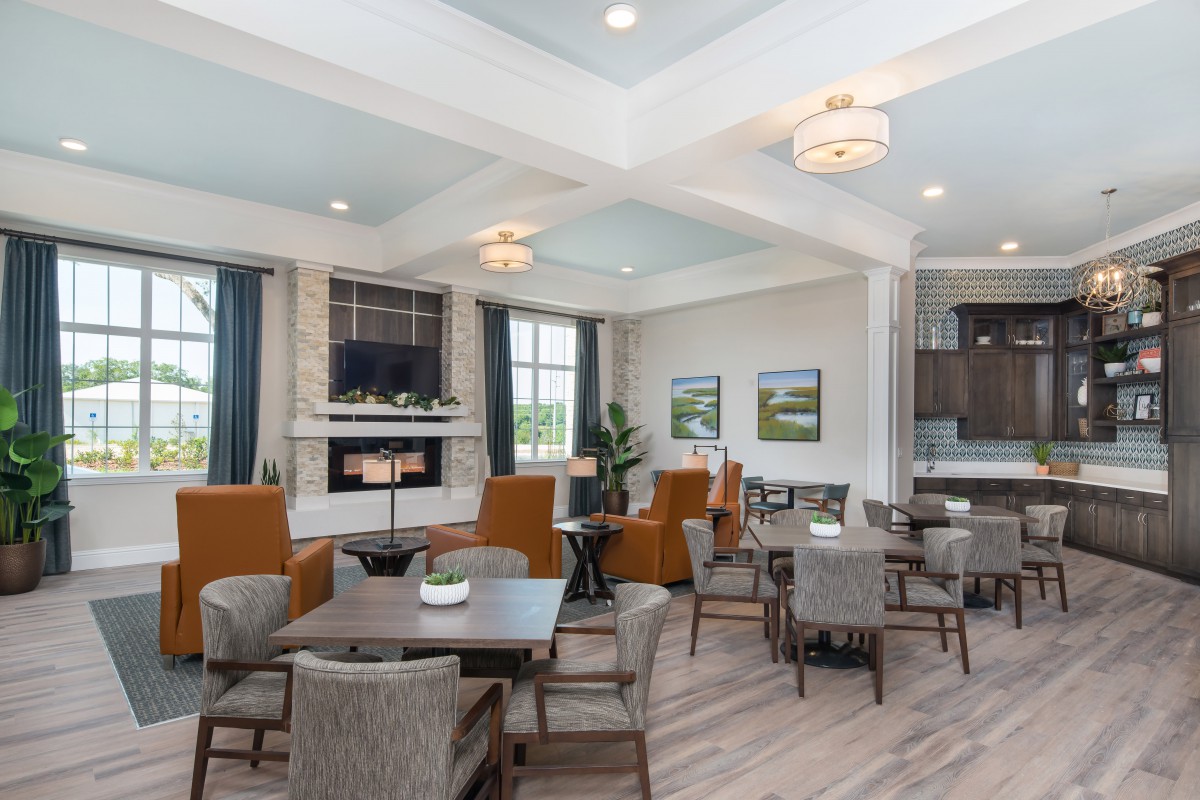 A modern living room with comfortable seating, tables, and a fireplace, illuminated by natural light from large windows.