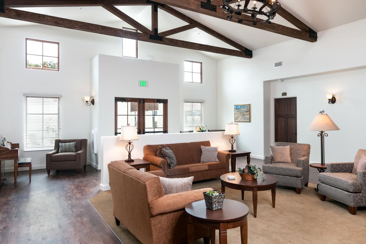 A well-lit living room featuring comfortable sofas, wooden coffee tables, and exposed ceiling beams.