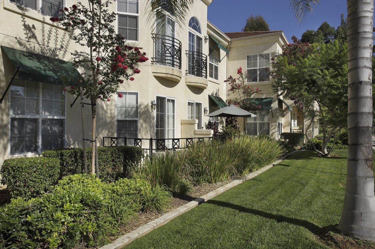 A sunny view of a residential apartment complex with well-maintained gardens and balconies.