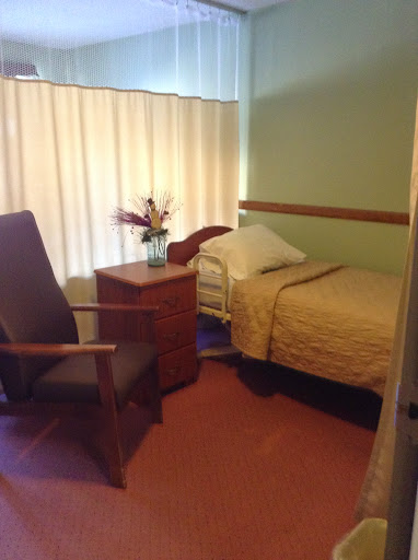 A view of a cozy hospital room featuring a bed, chair, and decorative flowers.