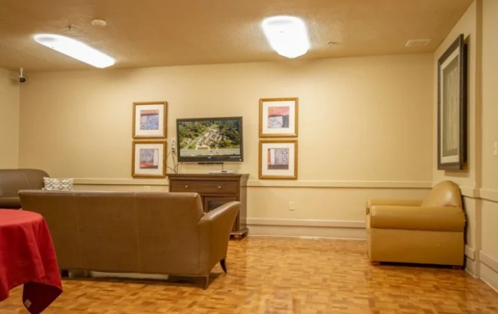 A cozy living room with a television and framed artwork on the wall, featuring comfortable sofas and a wooden floor.