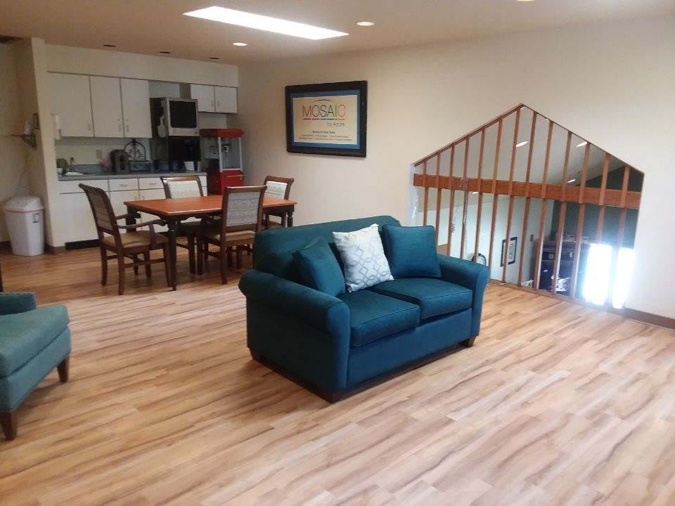 A cozy living and dining area with a teal sofa, wooden floors, and an open kitchen space.