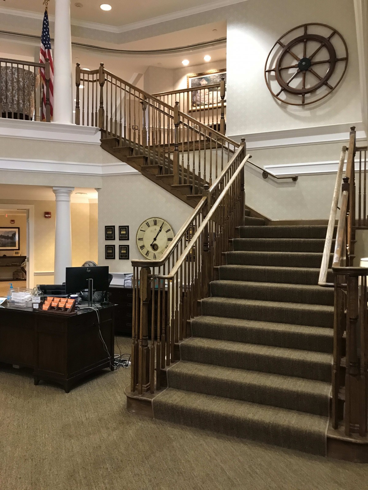 A spacious lobby with a prominent staircase and large wall clock.