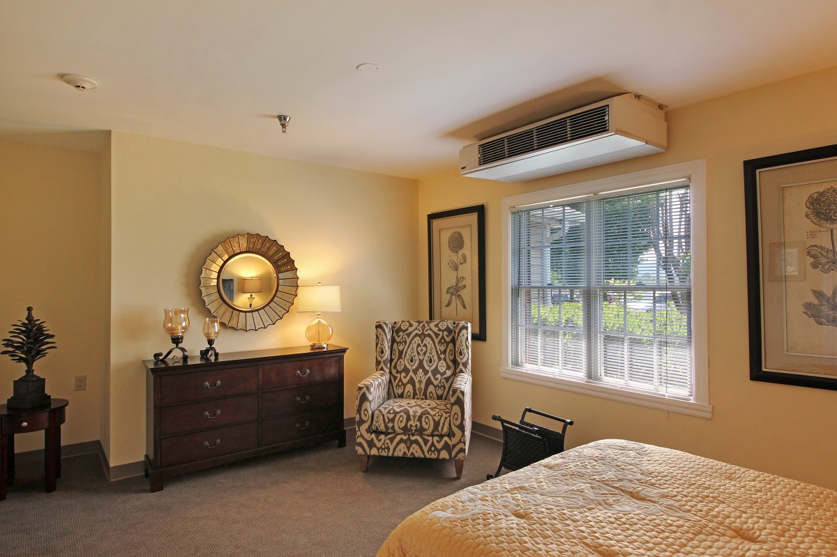 A cozy bedroom with a dresser and an upholstered armchair near the window.