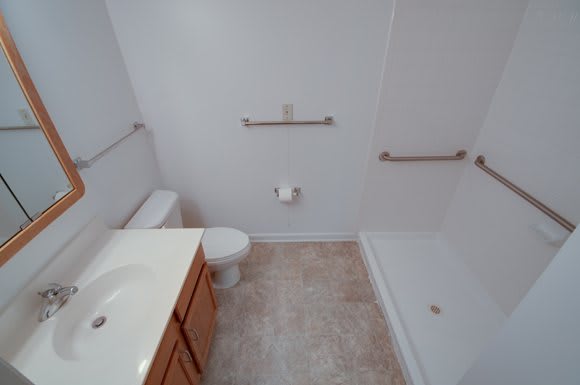 A clean and simple bathroom with a toilet, sink, shower, and cabinets.