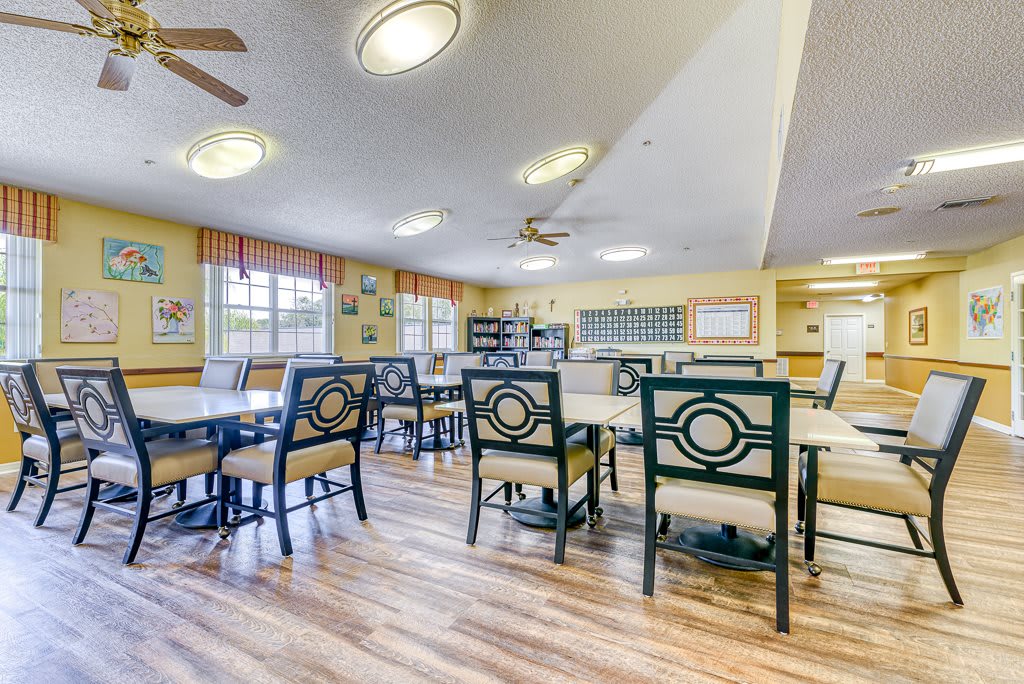 A spacious dining room with multiple tables and chairs, featuring large windows and wooden flooring.