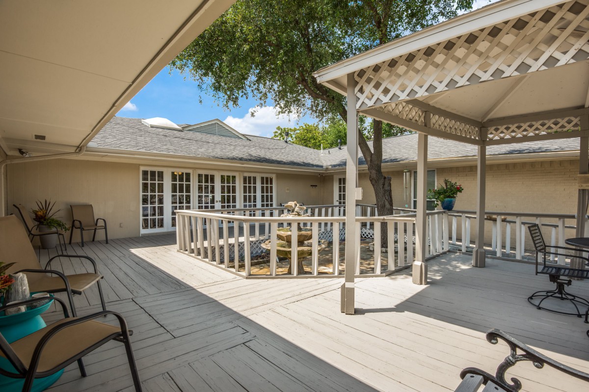 A spacious outdoor patio with a wooden deck, featuring comfortable seating arrangements and a gazebo, surrounded by trees.