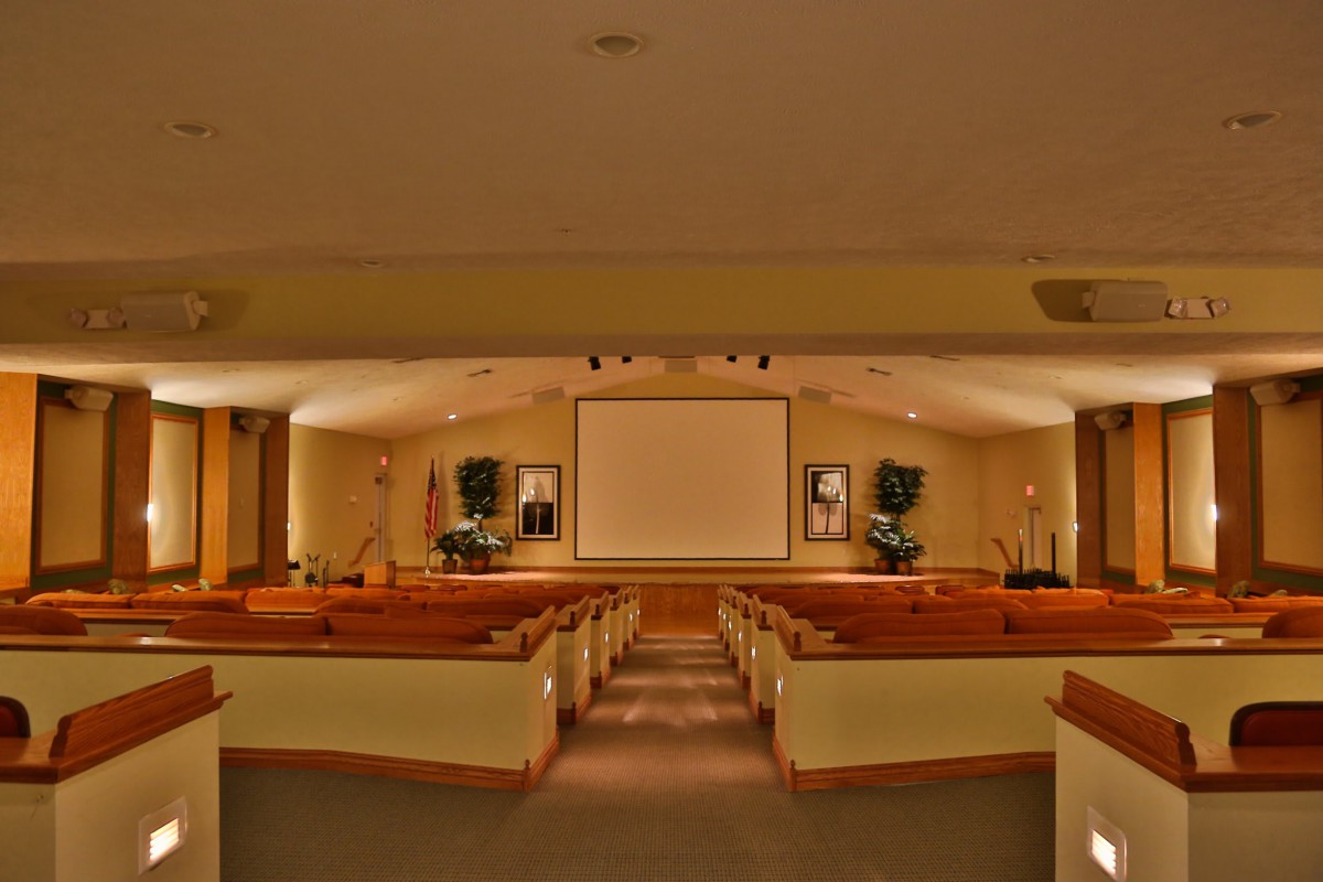 An empty church auditorium with rows of wooden pews and a large screen at the front.