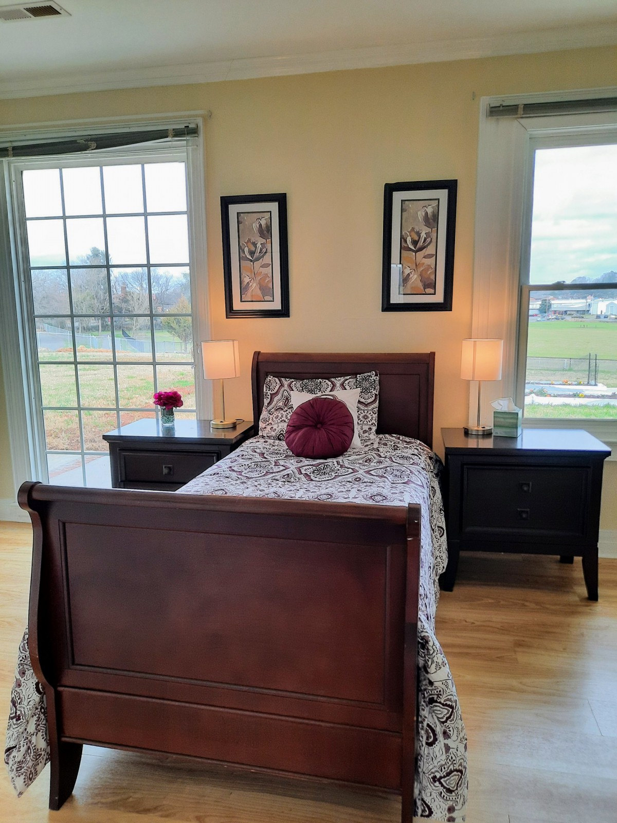 A cozy bedroom with a single bed, two nightstands, and large windows providing ample daylight.