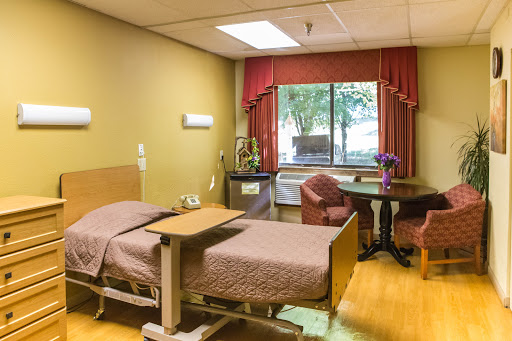 A cozy hospital patient room featuring a bed, seating area, and window with natural light.