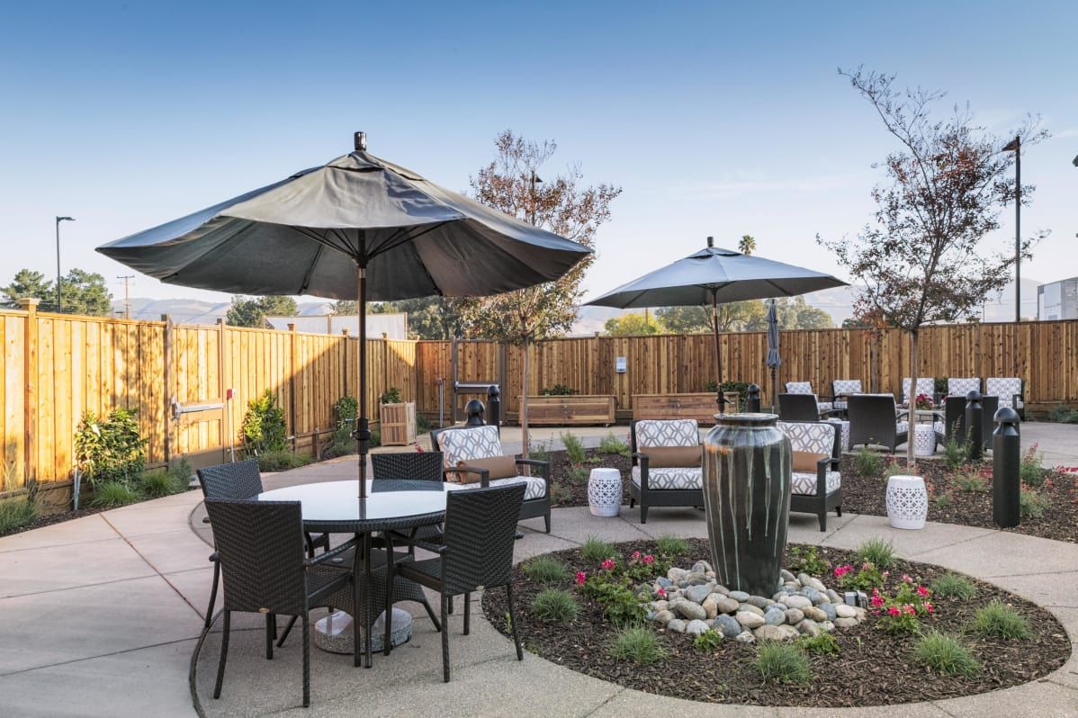 A modern outdoor patio area with tables, chairs, and umbrellas surrounded by landscaped garden features.