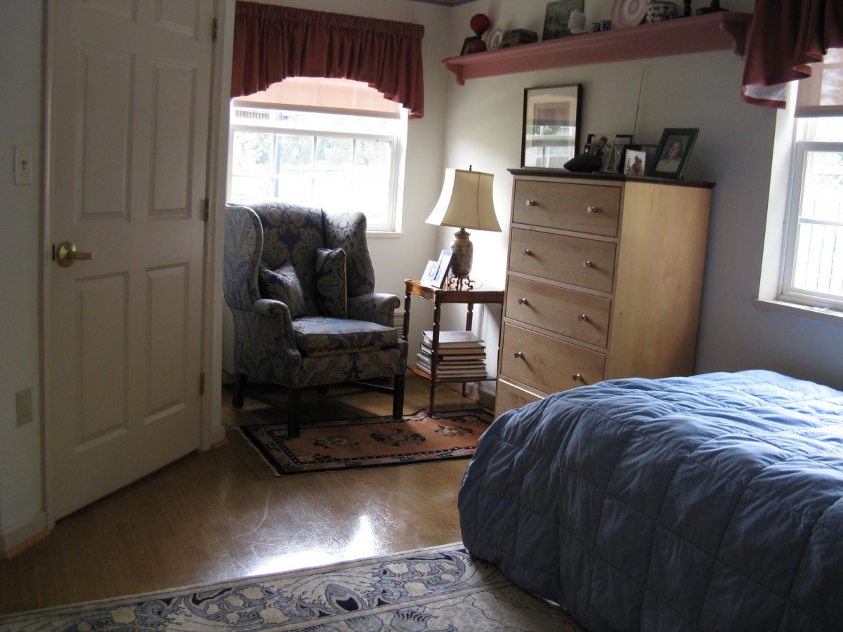 A cozy bedroom corner with an armchair, dresser, and a lamp by the window.
