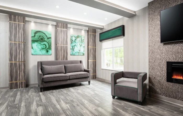 A modern living room with a grey sofa and armchair, complemented by abstract artwork and ample natural light.