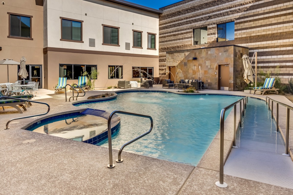 An outdoor swimming pool surrounded by modern buildings and deck chairs.