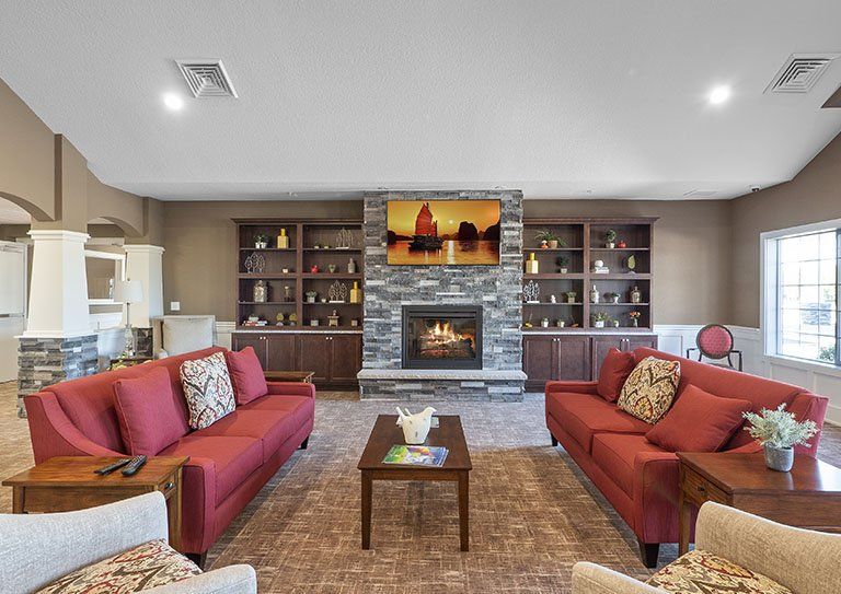 A cozy living room with red sofas facing a stone fireplace, surrounded by bookshelves.