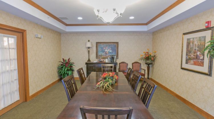 A formal dining room with a long wooden table, surrounded by chairs and accentuated by a chandelier and decorative elements.