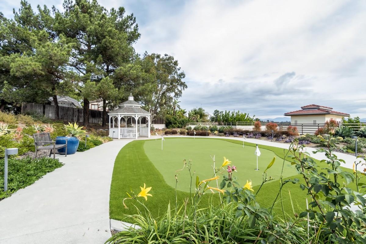 A beautifully landscaped garden featuring a gazebo, vibrant green grass, and blooming flowers under a partly cloudy sky.