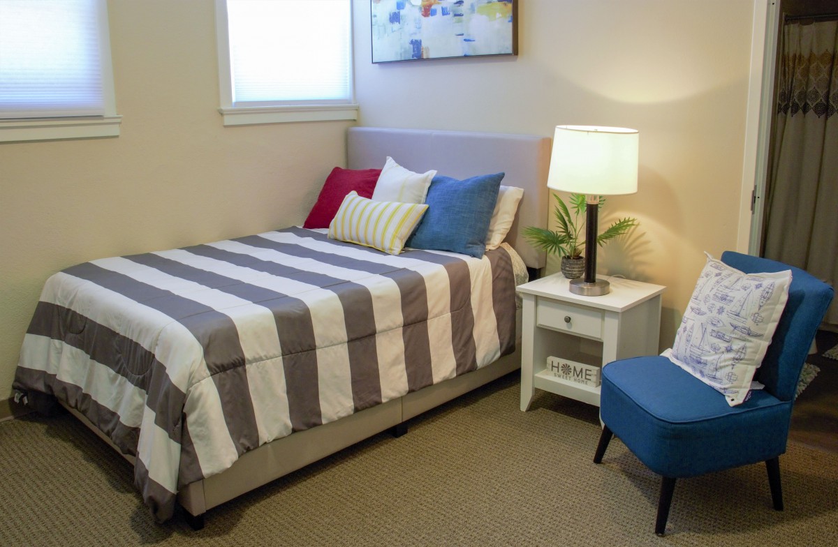 A cozy bedroom with a striped bedspread, colorful pillows, a nightstand with a lamp, and simple decor.