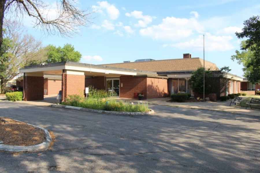 A one-story brick building with a driveway surrounded by trees under a blue sky.