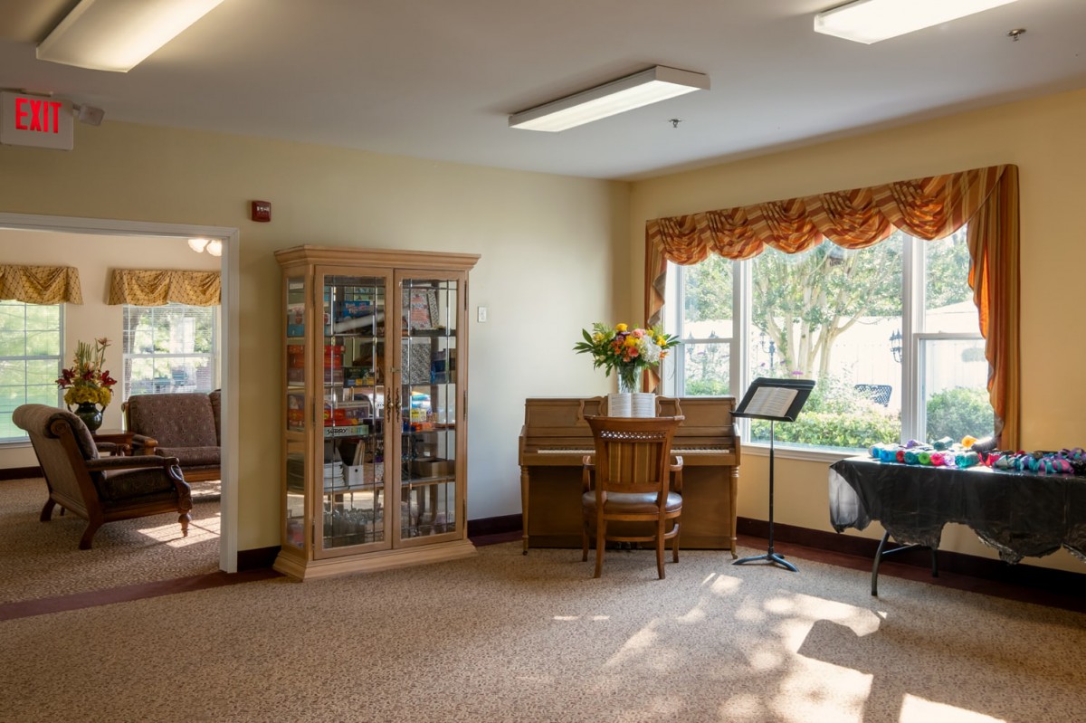 A cozy living space with a piano and bookshelf, illuminated by sunlight streaming through the window.