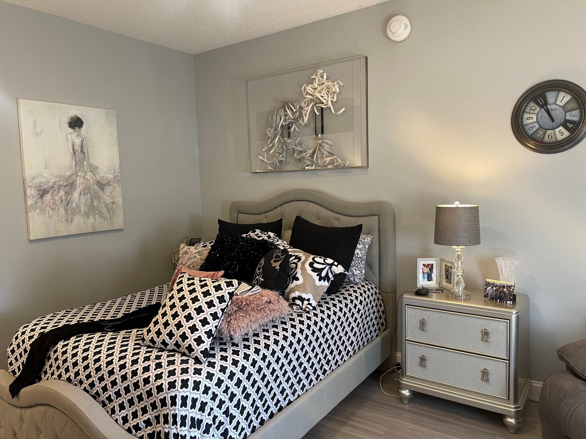 A stylishly decorated bedroom with a patterned bedspread, multiple pillows, and elegant artwork on the walls.