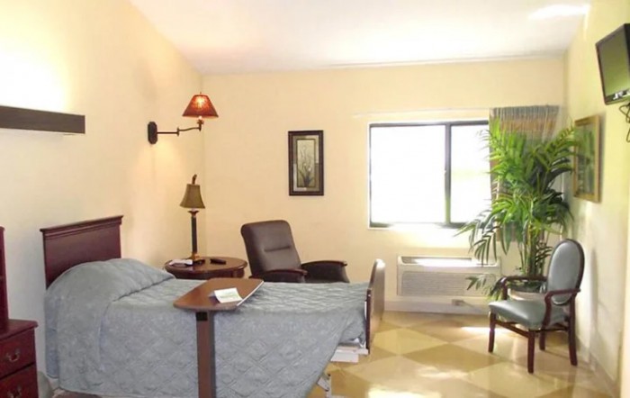 A cozy bedroom with twin beds, a lamp, chair, and a large window allowing natural light.