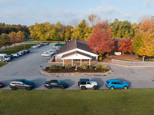 Aerial view of a building surrounded by autumn trees and a busy parking lot.