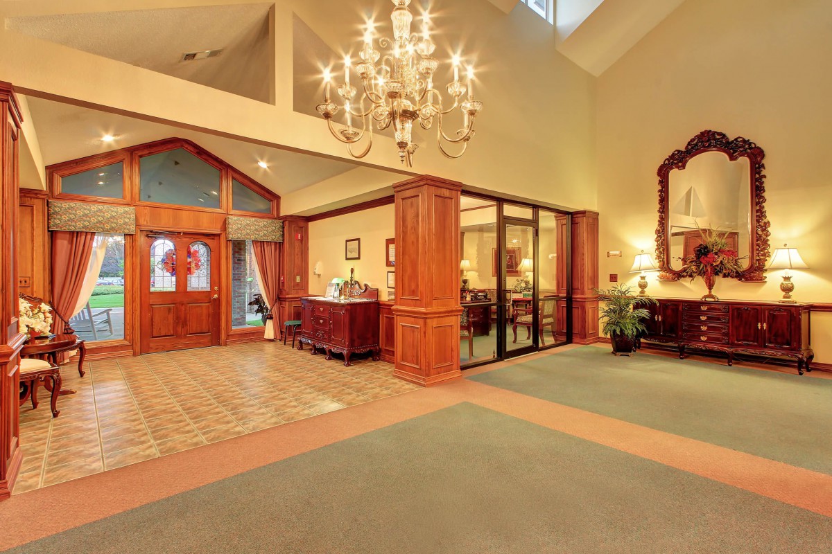 A spacious lobby with a chandelier, wood paneling, and a reception area.