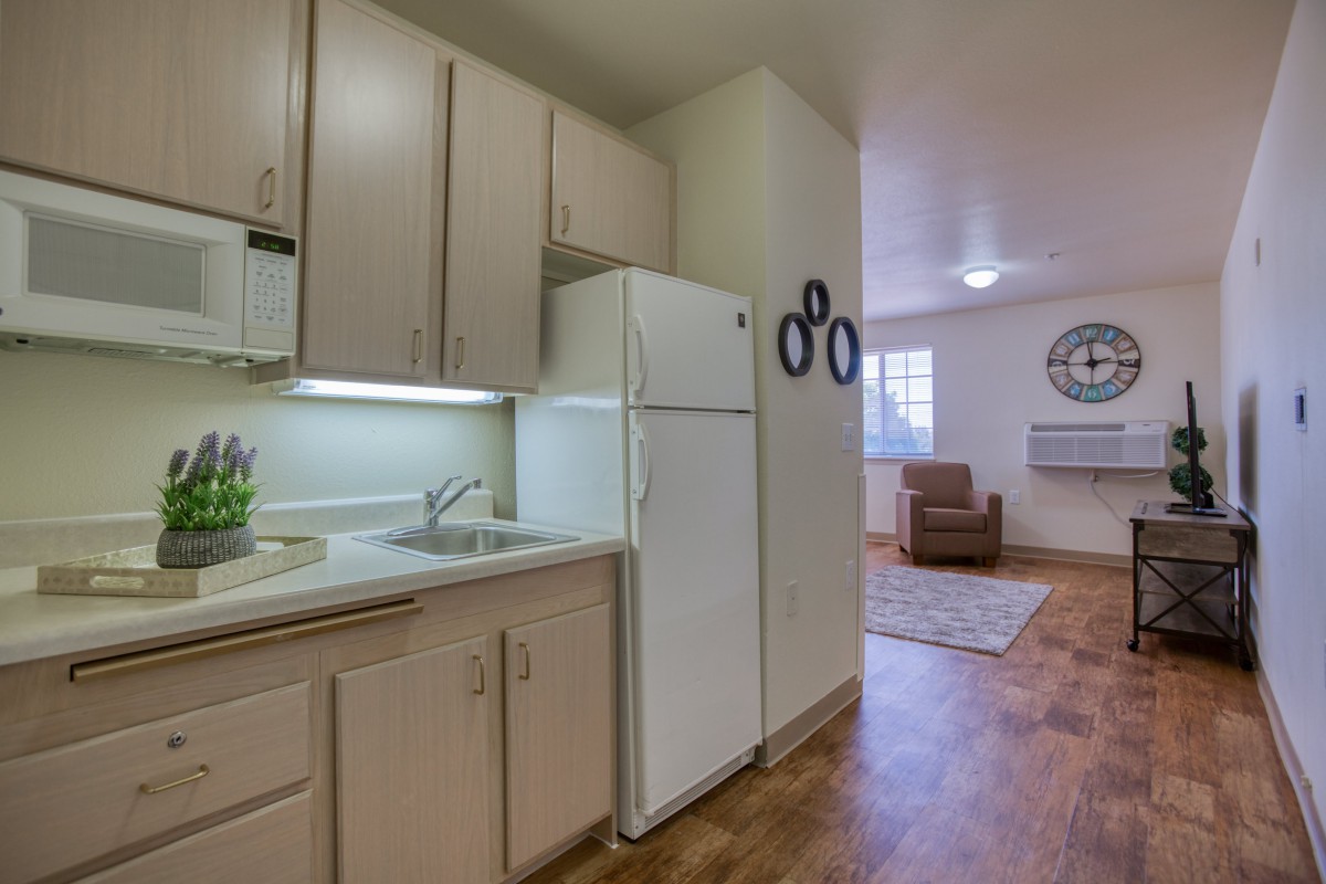A cozy apartment with a small kitchen featuring white cabinets and a refrigerator, opening into a living area with hardwood flooring.