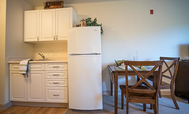 A cozy kitchen with a white refrigerator next to a wooden dining table and chairs.