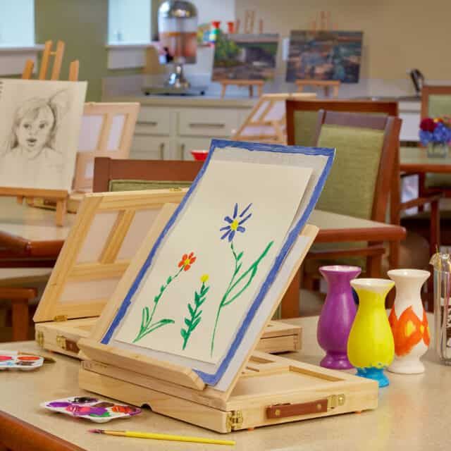 A cozy art studio with a watercolor painting of flowers on an easel, surrounded by art supplies.