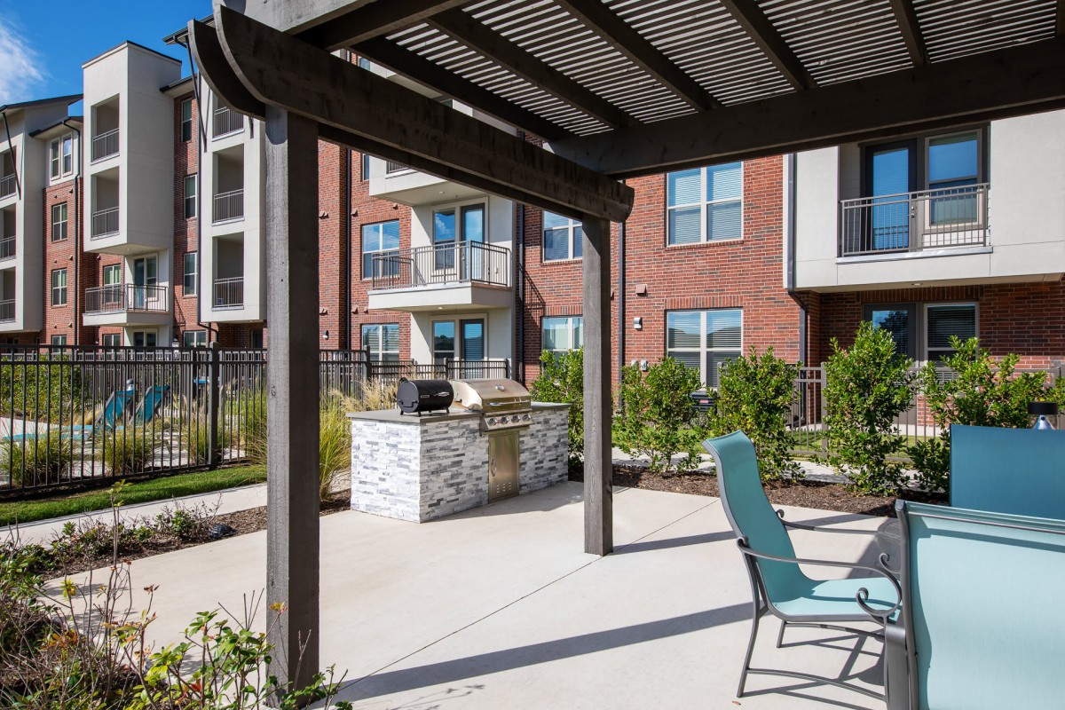 A modern apartment complex with an outdoor patio area featuring a pergola and seating.