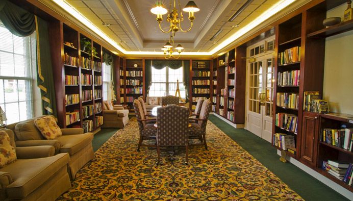 A cozy library room with bookshelves, a large table, and comfortable chairs.