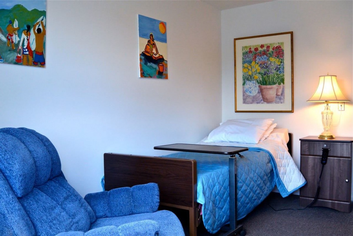 A room with a hospital bed and a blue armchair, decorated with artwork on the walls.