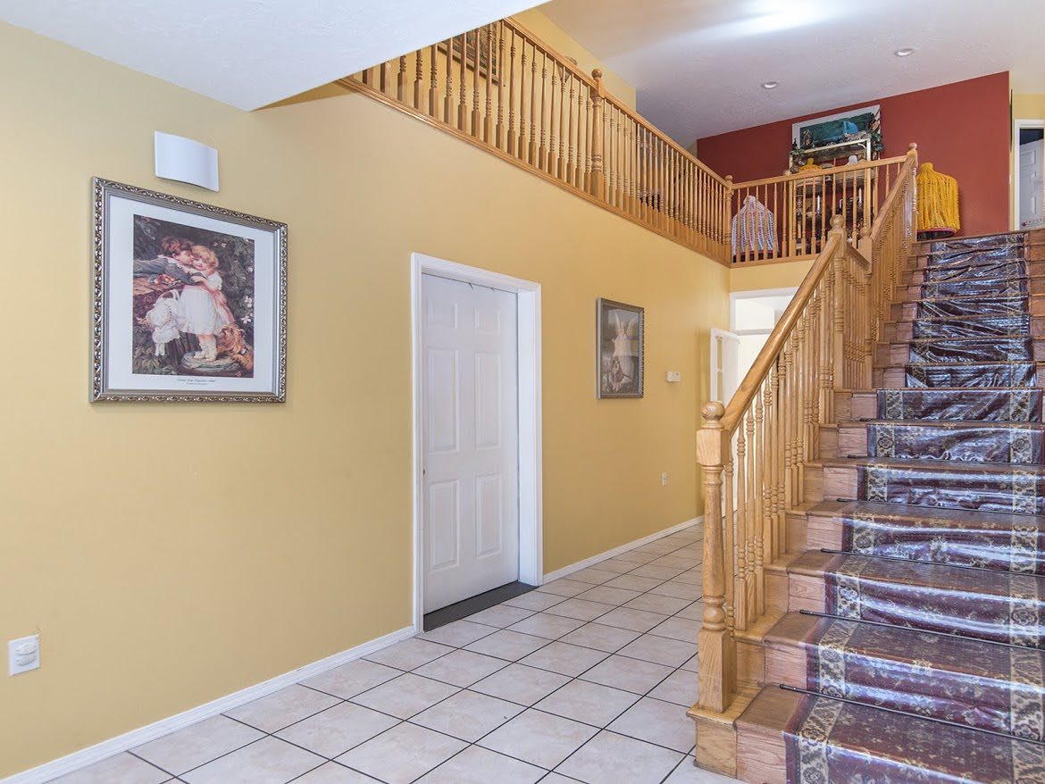 A bright hallway featuring a staircase with wooden railings and tiled flooring, adorned with wall paintings.
