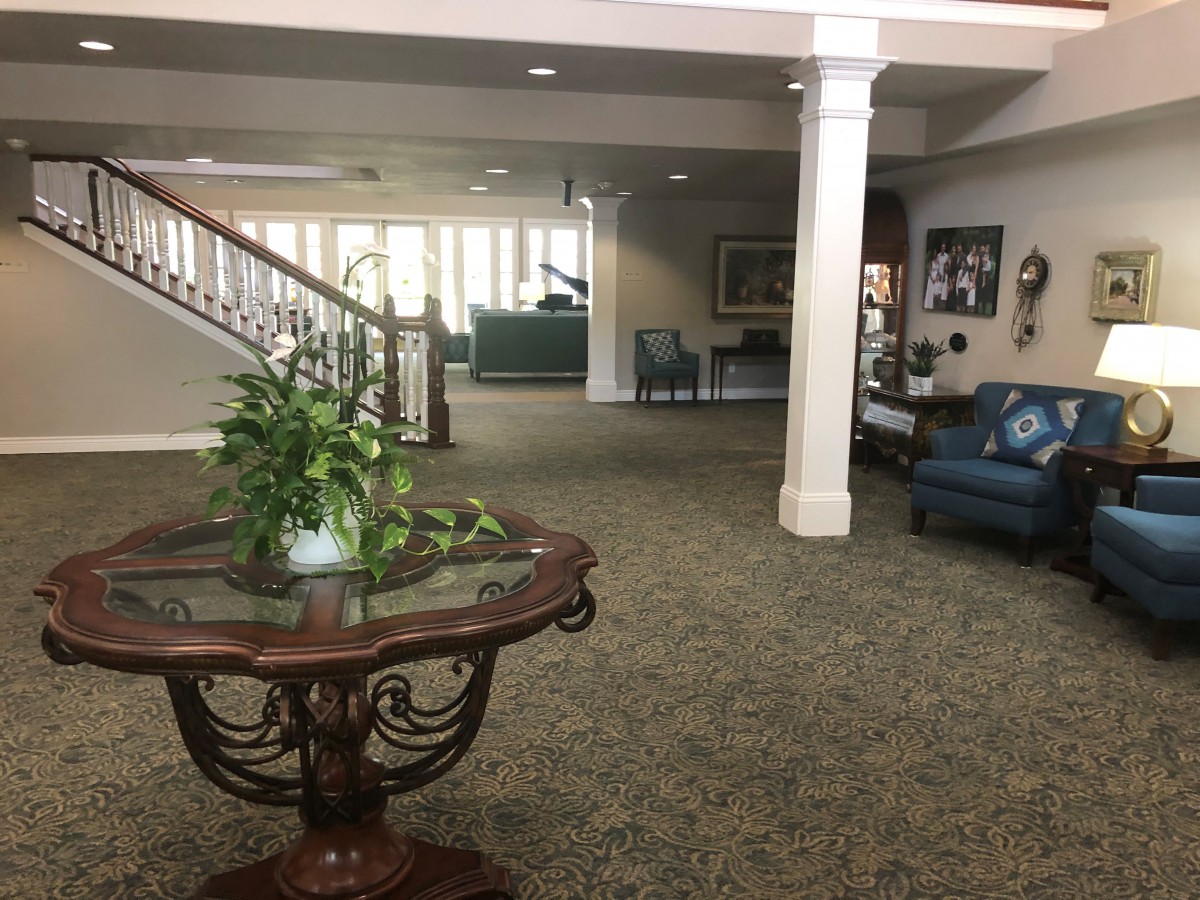 A spacious lobby with elegant decor, featuring a wooden table with plants, armchairs, and a staircase leading to the upper level.