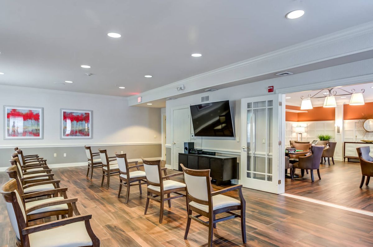 A modern living room with chairs arranged facing a large television on the wall.