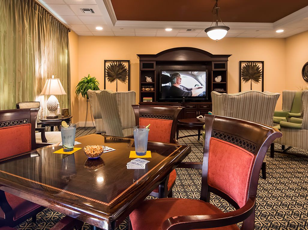 A cozy living room with a large table, chairs, and a television in the background.